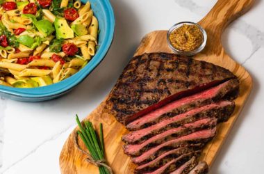 flank steak on a cutting board with a bowl of pasta salad