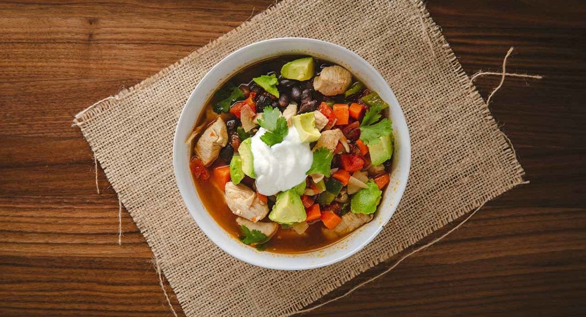 chicken and black bean soup in a white bowl with sour cream and avocado