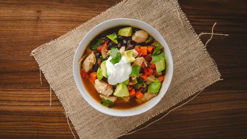 chicken and black bean soup in a white bowl with sour cream and avocado