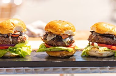 three beef cheeseburgers with lettuce and tomato on board