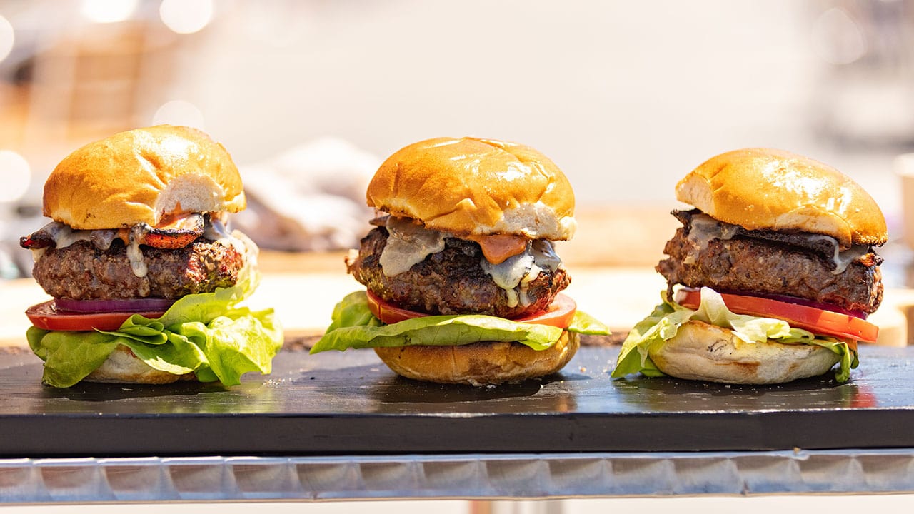 three beef cheeseburgers with lettuce and tomato on board