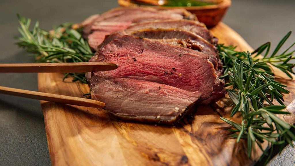 a sliced cut of cooked lamb with rosemary sprigs