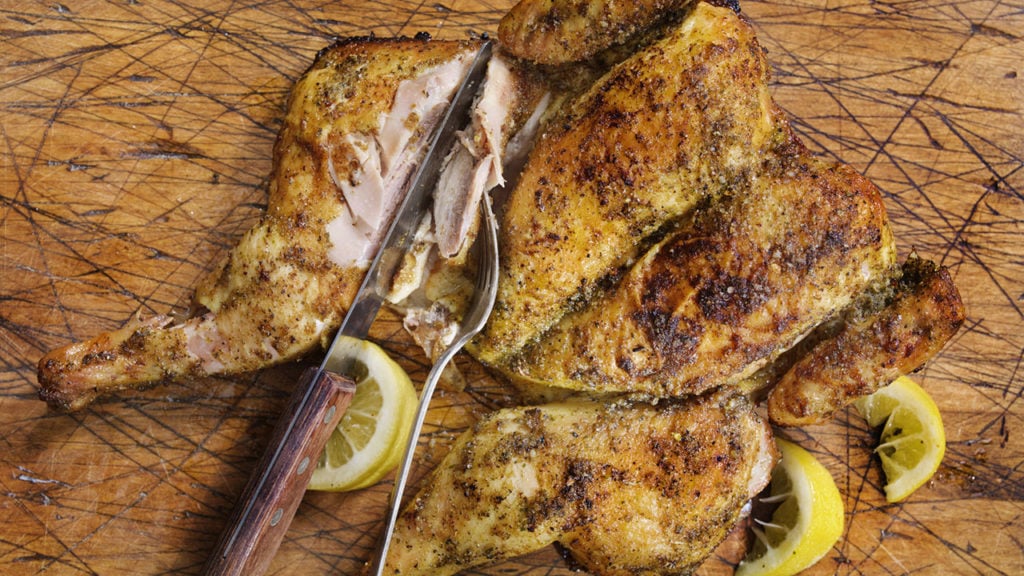 baked whole chicken with lemons on cutting board