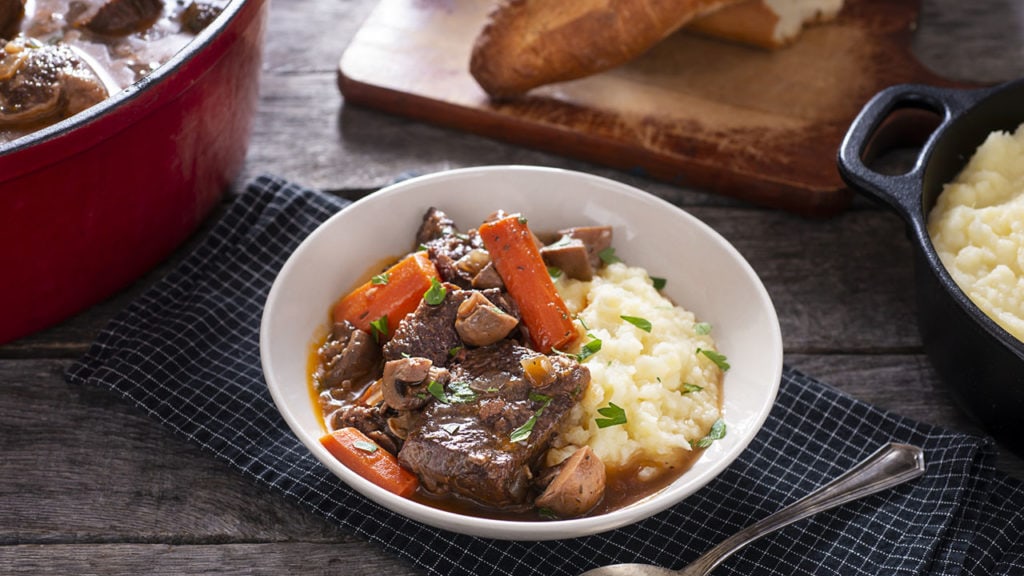 beef bourguignon in a bowl with bread and potatoes
