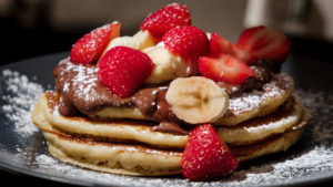 pancakes with hazelnut spread, powdered sugar, sliced bananas, and strawberries