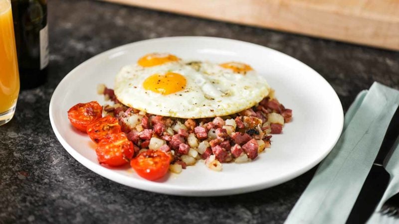 an egg on top of corned beef hash on a plate on top of a breakfast table