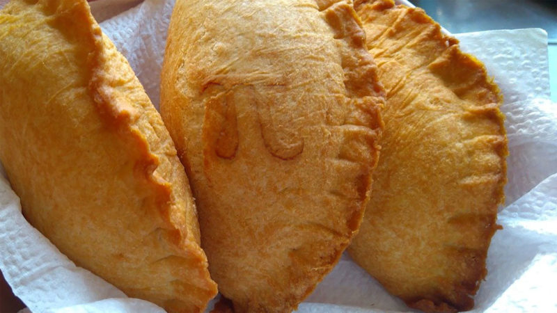 Three meat hand pies on a paper towel with a pi symbol on one of them