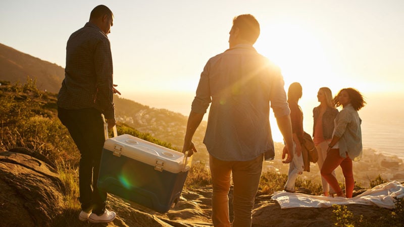 A group of people carrying a cooler with the sun shining