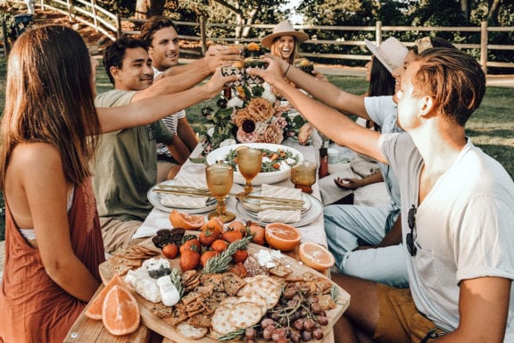 people raising their glasses around a picnic table with food on it