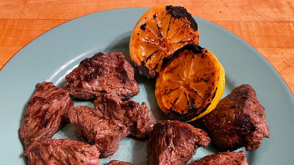 steak tips on a plate with charred lemon halves
