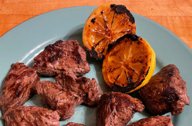 steak tips on a plate with charred lemon halves