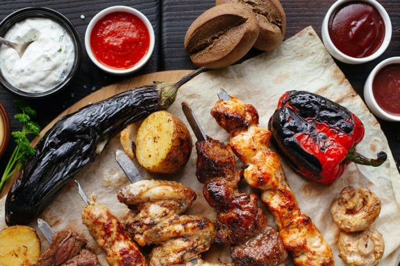 Skewered meat on a table with different hot sauces and dips in ramekins