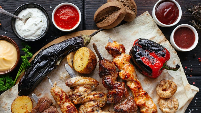 Skewered meat on a table with different hot sauces and dips in ramekins