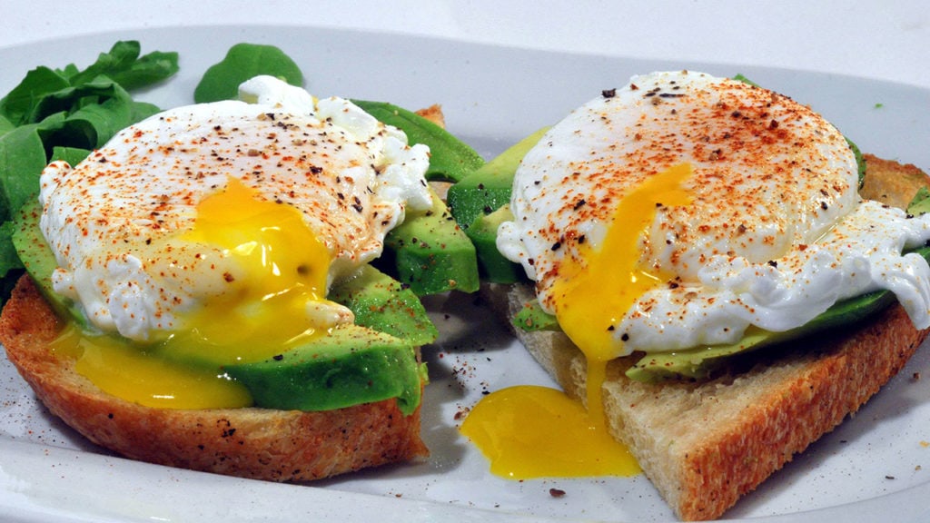 two slices of toast topped with avocado and poached eggs