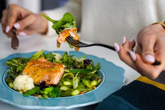 person eating salmon on top of vegetables with a fork and knife