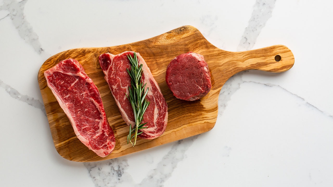 three cuts of raw beef on a cutting board
