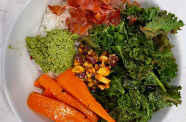 rice topped with roasted kale, carrots, proscuitto, hazelnuts, and basil pesto in a bowl