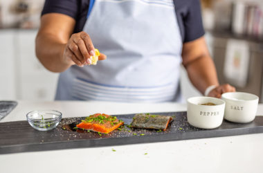 Person squeezing a lemon onto salmon filets on a cutting board with salt and pepper