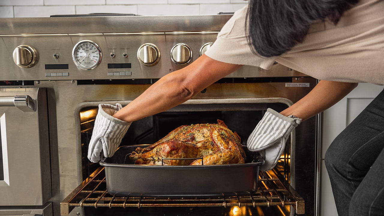 person placing a turkey in a roasting pan in the oven