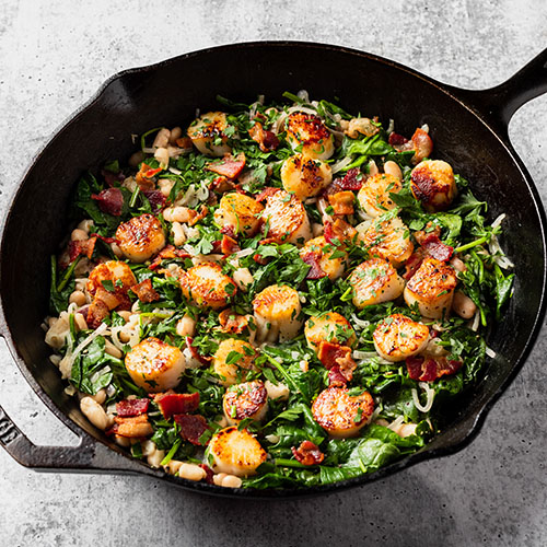 skillet with spinach scallops bacon and beans