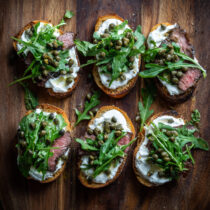Filet Crostini with Horseradish Cream, Arugula and Capers on a chopping board