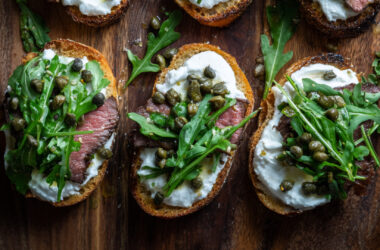 Filet Crostini with Horseradish Cream, Arugula and Capers on a chopping board