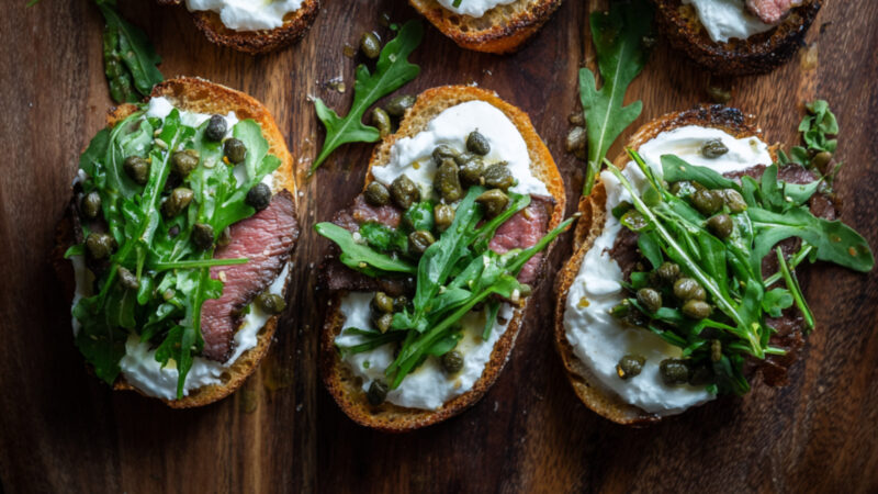 Filet Crostini with Horseradish Cream, Arugula and Capers on a chopping board