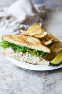 a plate with a pickle, chips, and half a tuna salad sandwich