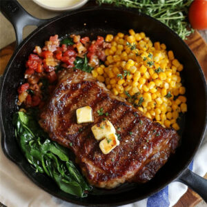 ny strip steak with butter on top next to corn and vegetables at the side